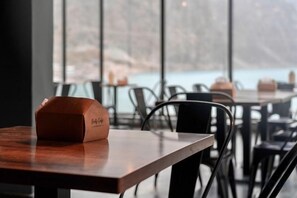 Interior de restaurante con mesas y sillas, vista al exterior y una bolsa de papel sobre una mesa.