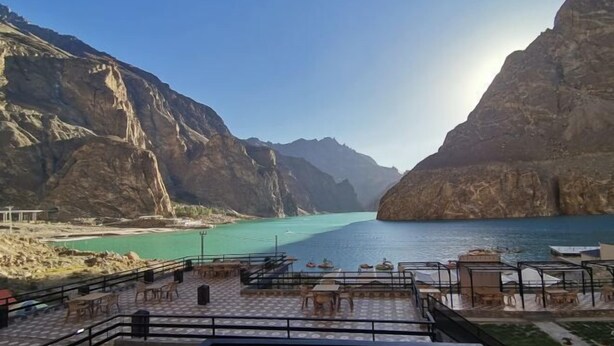 A terrace with tables and chairs overlooking a calm lake surrounded by rocky cliffs.