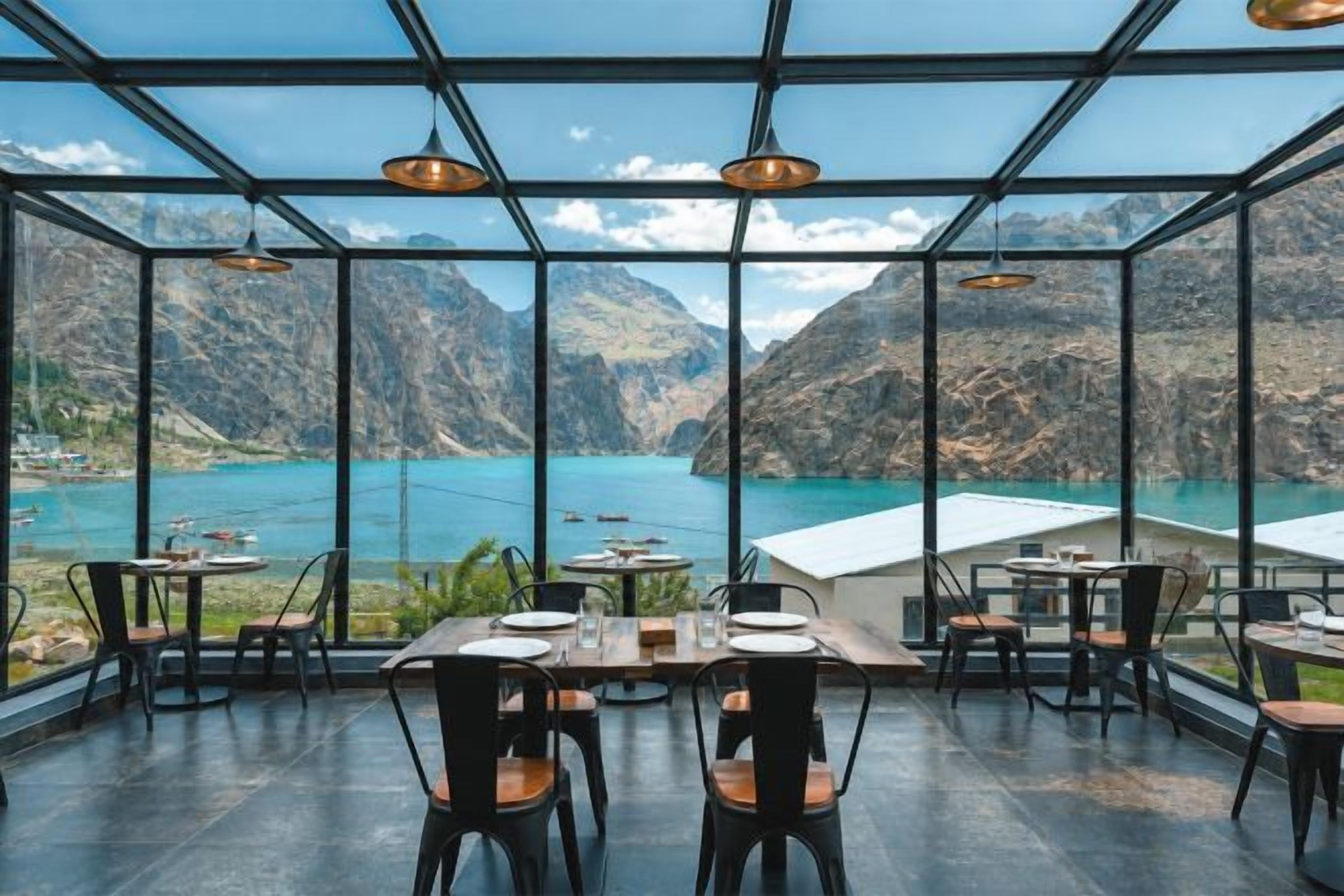 An indoor dining area with tables and chairs, large windows, and a view of a lake and mountains.