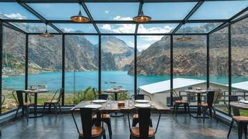 An indoor dining area with tables and chairs, large windows, and a view of a lake and mountains.