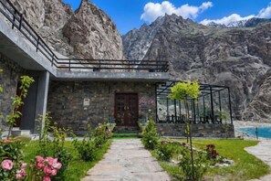A stone building with a glass conservatory, a red door, and a pathway leading to a mountain view. - Horizon Resort Hunza (Gilgit)