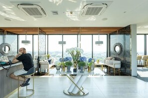 A modern office space with a large desk, a chair, a table with a vase of flowers, and a view of the city through large windows. - Sky RiverPool, Cozy & Luxury for family (Chiang Mai)