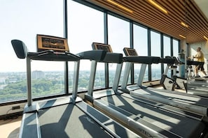 A gym with treadmills and exercise equipment, large windows with a city view, and a wooden ceiling. - Sky RiverPool, Cozy & Luxury for family (Chiang Mai)
