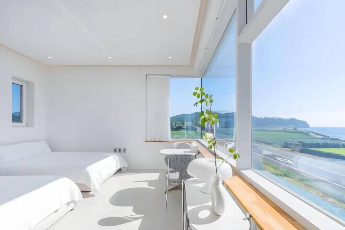A modern hotel room with a large window, a bed, a small table, and a chair.