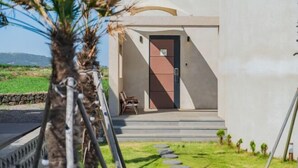 Un edificio moderno con una entrada minimalista, escalones que conducen a una puerta y un pequeño área de descanso con sillas.
