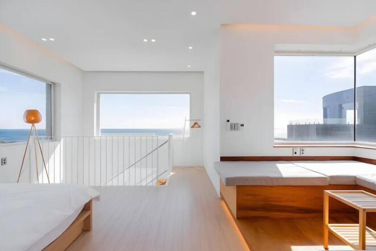 A modern room with a large window, a wooden floor, a bed, a bench, and a table.
