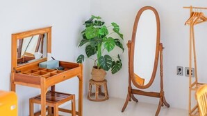 Una habitación con un escritorio de madera, un espejo, una planta en maceta y un caballete de madera.
