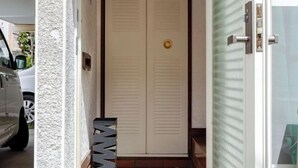 A hallway with a white door, a textured wall, and a car parked outside. - Yokohama Chuo 2 House (Yokohama)