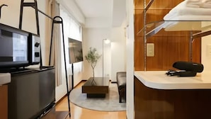 Habitación de hotel moderna con televisor de pantalla plana, sofá, mesa de centro y repisa de vidrio con toallas.