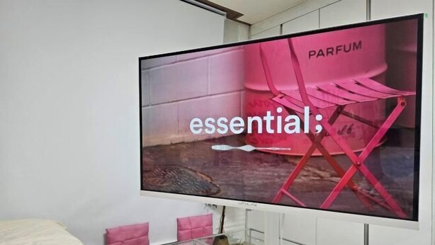A television displaying an advertisement for a perfume brand, with a pink chair and a brick wall in the background. - 3 minutes Seoul Station by AREX from Incheon Airport, luggage storage breakfast included (Seoul)