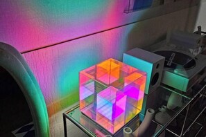 Una mesa de vidrio con un centro geométrico colorido, un florero blanco y una planta pequeña sobre un estante de vidrio.