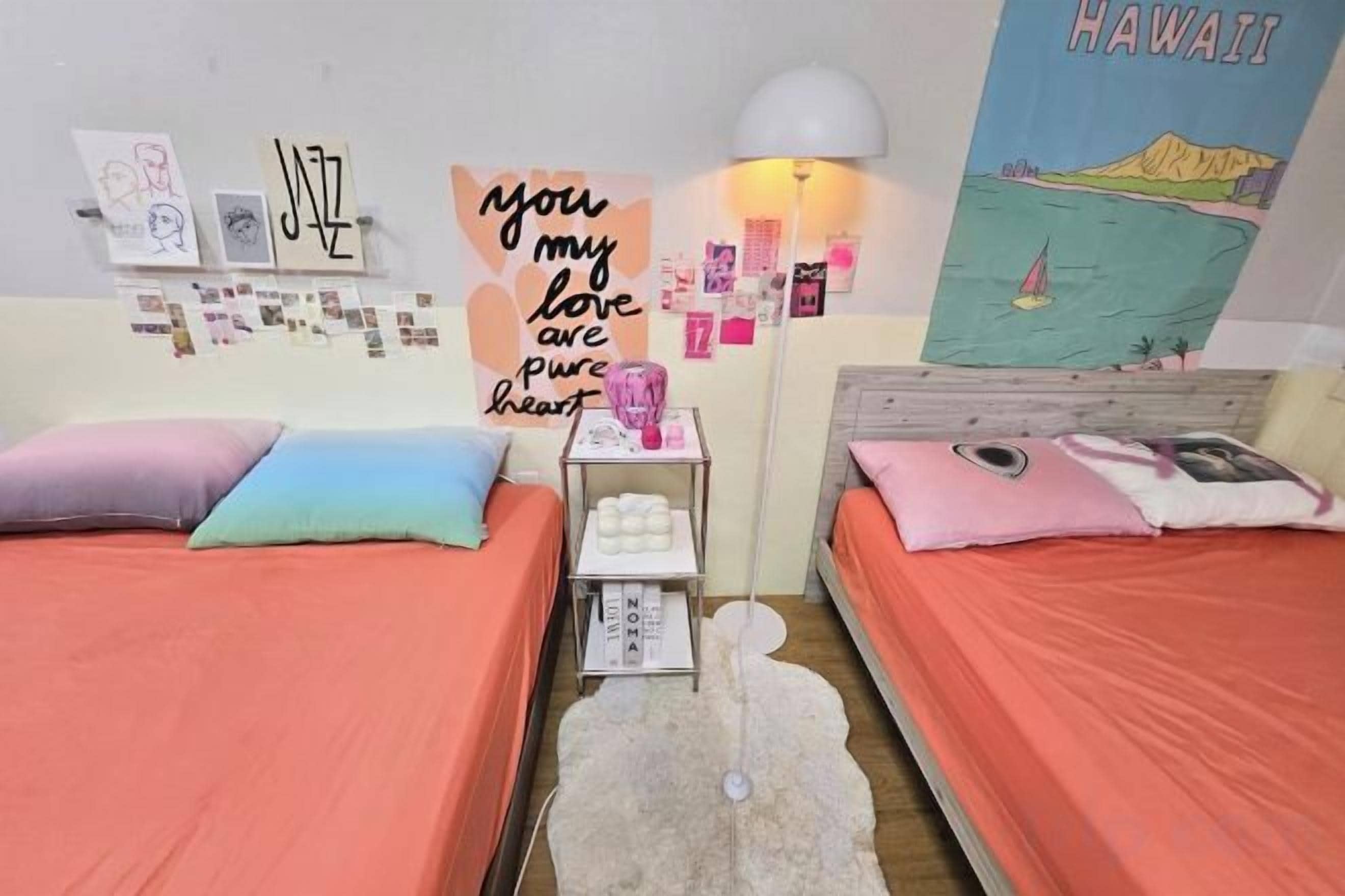 Une chambre avec deux lits, une table de chevet, des œuvres d’art murales et une affiche.