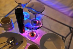 Una mesa con una copa de vino de vidrio, un vaso negro y un plato blanco con cubiertos.