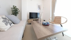 Ένα μοντέρνο σαλόνι με έναν καναπέ, ένα ξύλινο τραπεζάκι σαλονιού, μια τηλεόραση και μια καρέκλα από μπαμπού.