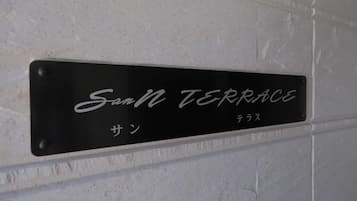 A black metal sign with white lettering on a white wall, reading 'San TERRACE' with additional text in another language below.