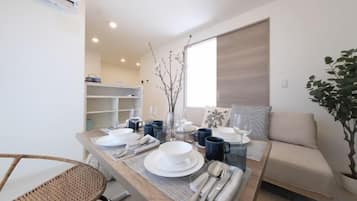 A dining area with a wooden table set for four, a sofa, and a potted plant.