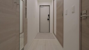 Ένας στενός, καλά φωτισμένος διάδρομος με μια πόρτα στο τέλος, πλακάκια στους τοίχους και ένα δάπεδο σε ανοιχτόχρωμο τόνο.