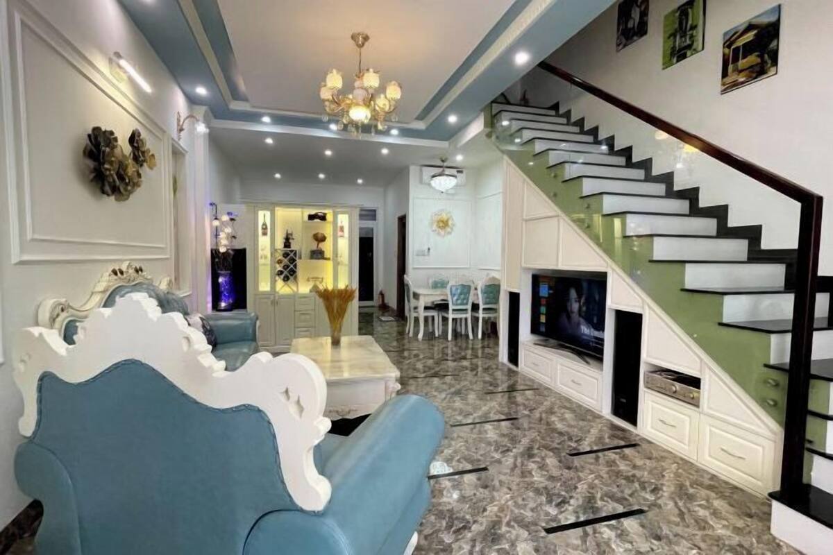 A modern living room with a sofa, a TV, a staircase, and a dining area.