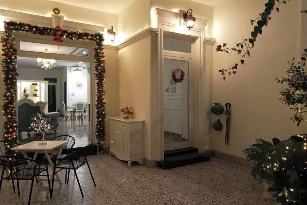 A room with a dining table, chairs, a white cabinet, a door with a wreath, and a Christmas tree.