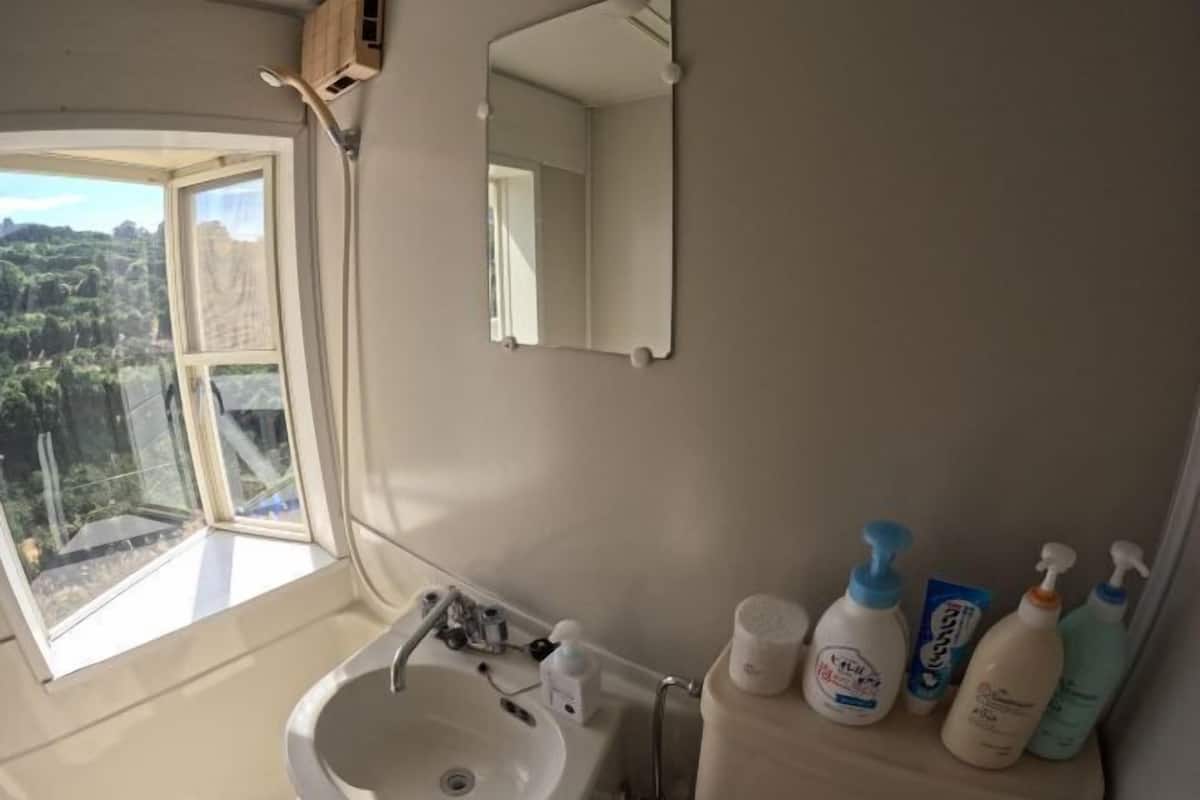 Une salle de bain avec une grande fenêtre, un lavabo, un miroir et des articles de toilette posés sur le comptoir.