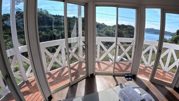 A sunroom with a view of a lake and hills, a wooden deck, and a lounge area with a towel and a book. - Ultra Private Off Grid Island Villa Near the Beach Mandarin Farm Setting (Bizen)