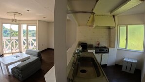 A room with a sofa, a small table, a kitchen area with a sink, and a window overlooking greenery. - Ultra Private Off Grid Island Villa Near the Beach Mandarin Farm Setting (Bizen)