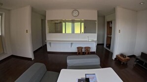 A modern living room with a large white sofa, a small table, and a large mirror above a built-in bench. - Ultra Private Off Grid Island Villa Near the Beach Mandarin Farm Setting (Bizen)