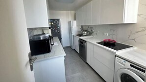 Cocina compacta con armarios blancos, horno empotrado, lavavajillas y lavadora.