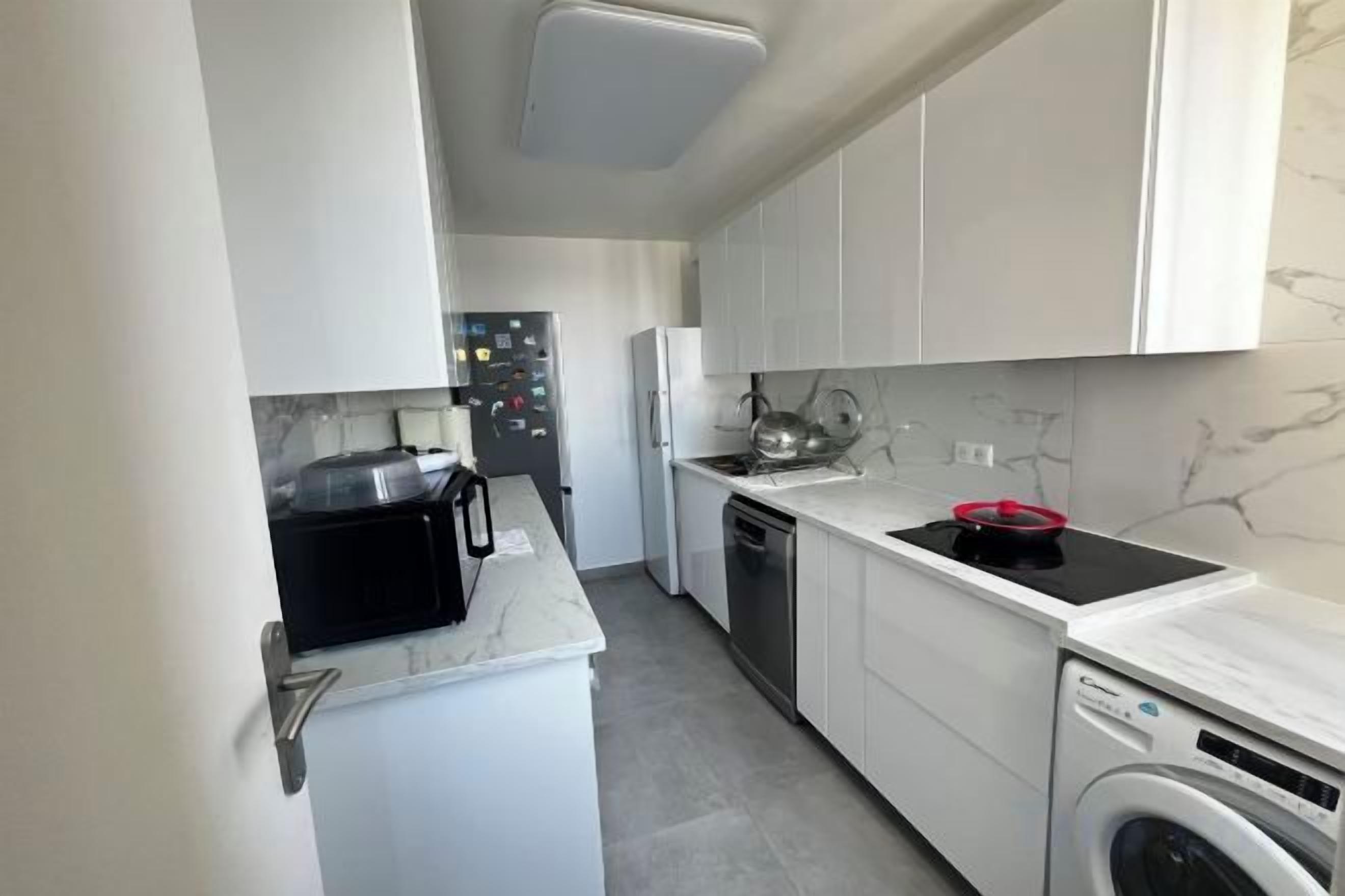 Une cuisine compacte avec des meubles blancs, un four à micro-ondes, un lave-vaisselle et une cuisinière.