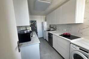 Una cocina compacta con armarios blancos, microondas, lavavajillas y estufa.