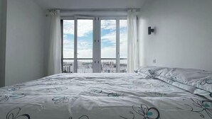 Un dormitorio con una cama grande, una ventana con cortinas y vistas a un paisaje urbano.