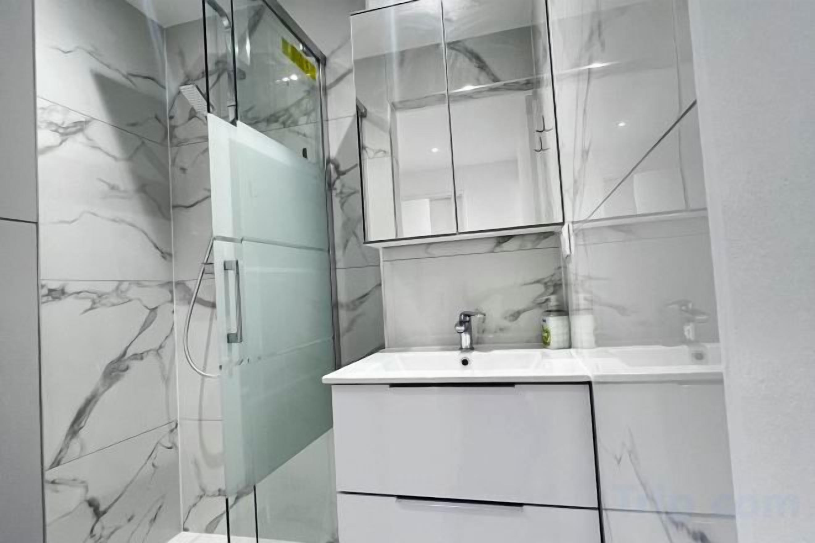 Une salle de bain moderne avec une douche à parois de verre, un lavabo blanc et des murs à motifs de marbre.