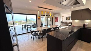 Una cucina moderna con una grande isola, un'area pranzo con tavolo e sedie, e vista sull'esterno.