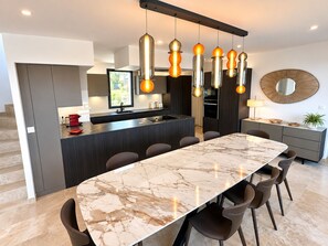 A modern kitchen with a central island, pendant lighting, and a marble dining table.