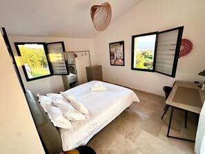 A bedroom with a bed, a desk, and two windows with blinds.