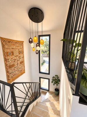 Eine moderne Treppe mit schwarzem Geländer, einer hängenden Leuchte und Blick ins Freie durch ein Fenster.
