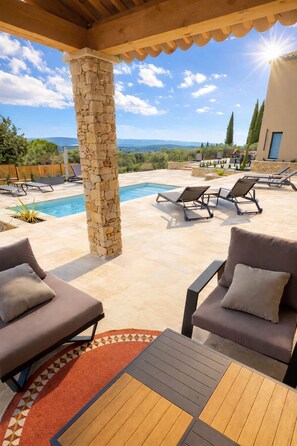 A poolside area with lounge chairs, a stone pillar, and a view of the landscape.