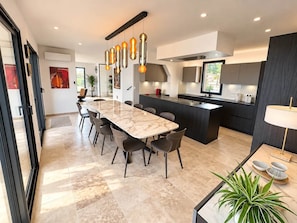 A modern kitchen with a central island, pendant lighting, and a dining area with a marble table. - Keur bouyo - Provençal Luxury Retreat (Saint-Saturnin-lès-Apt)