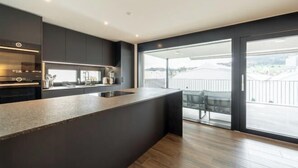 A modern kitchen with a large island, a built-in oven, and a view of the city through large windows.