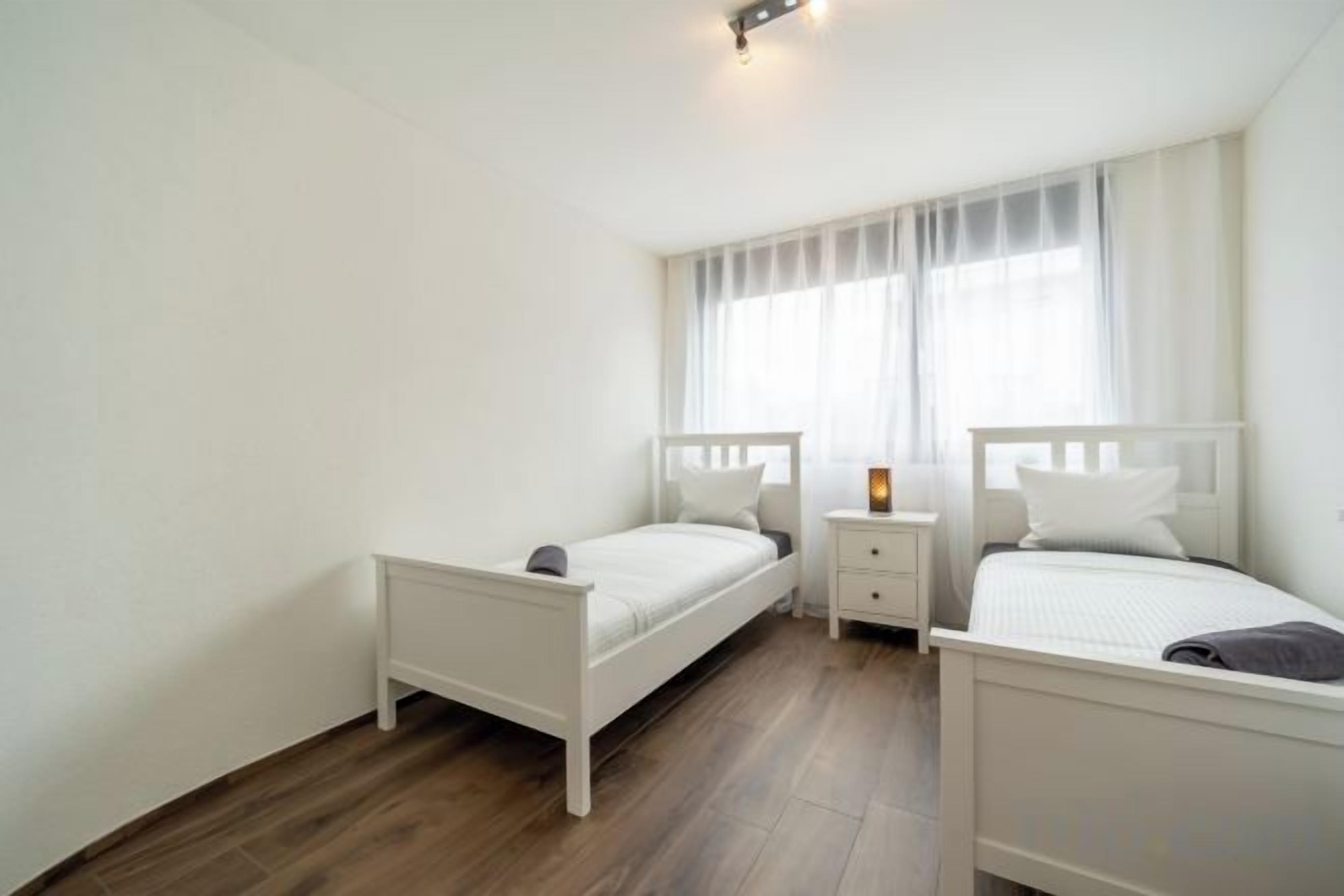 Une chambre avec deux lits simples, une table de chevet et une fenêtre avec des rideaux.