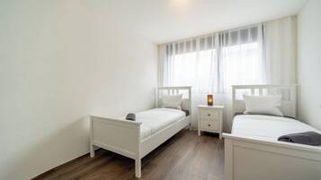 Une chambre avec deux lits simples, une table de chevet et une fenêtre avec des rideaux.