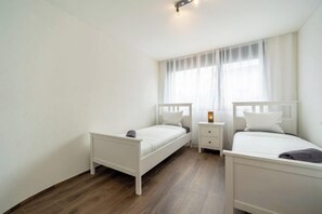A bedroom with two single beds, a nightstand, and a window with curtains. - Swiss Living High-Tech Kitchen, 1G WiFi, Balcony (Kulm District)