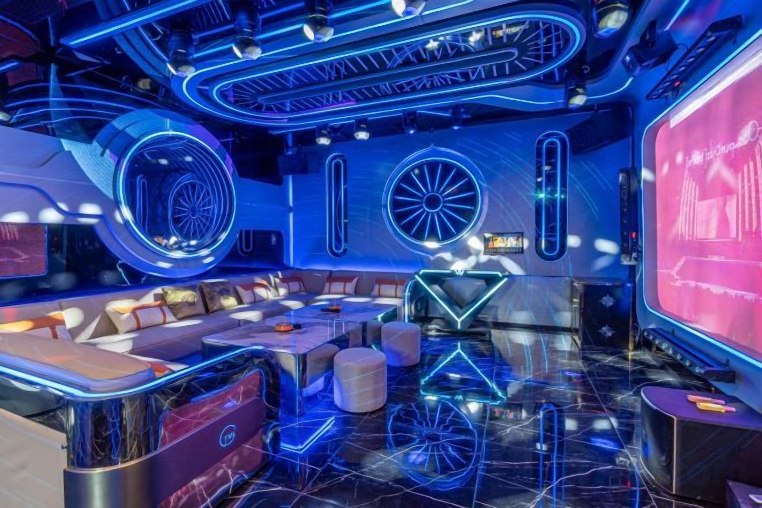 A modern interior with a bar area, seating, and a large screen displaying content.