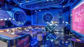 A modern interior with a bar area, seating, and a large screen displaying content.