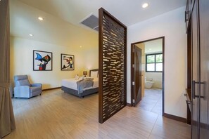 Quarto de hotel com cama, uma cadeira, uma escrivaninha e obras de arte nas paredes.