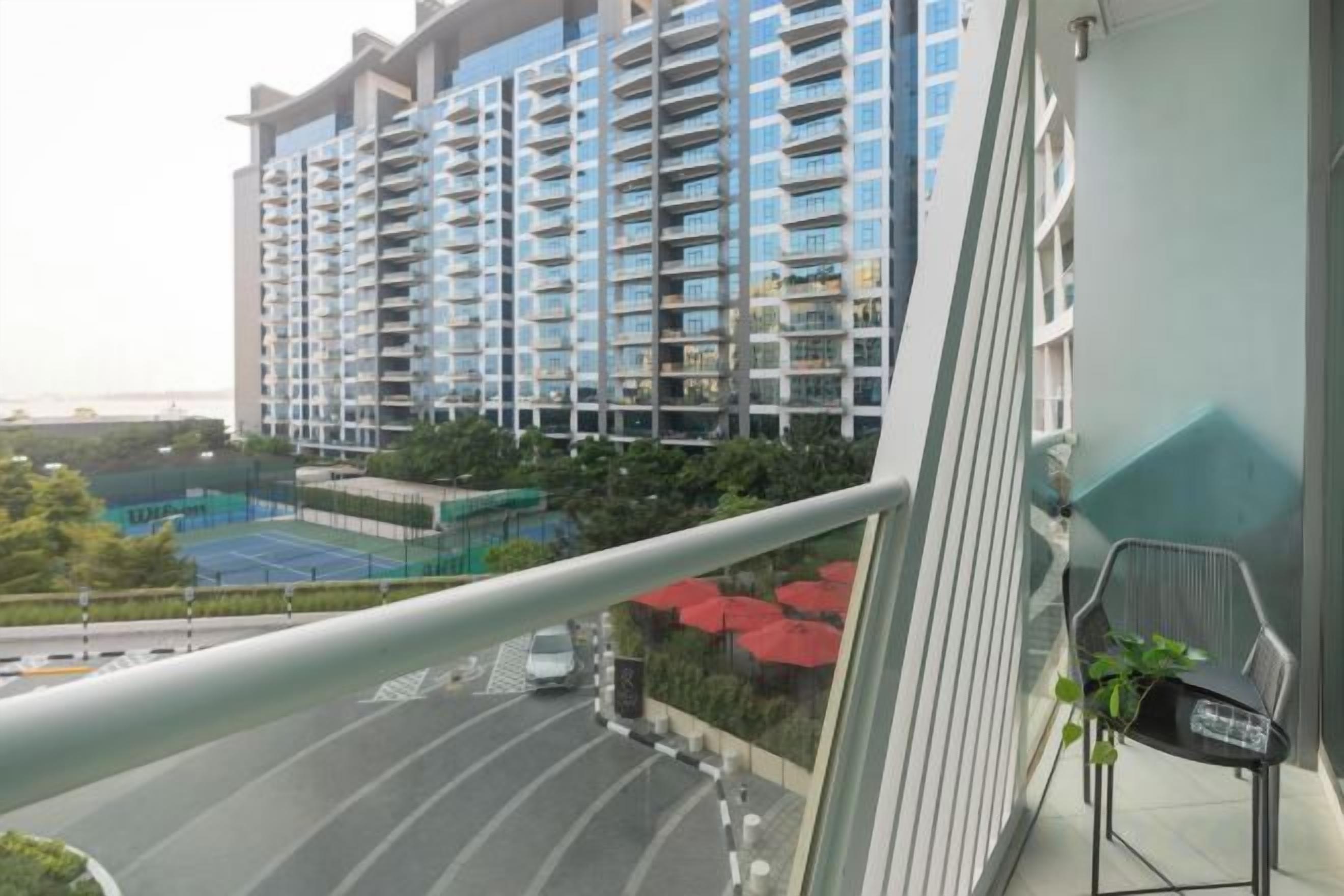 A high-rise building with multiple balconies, a tennis court, and a view of a road.