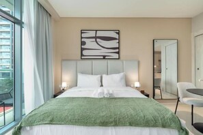 A hotel room with a large bed, two bedside tables with lamps, a green throw blanket, a large mirror, and a view of a building outside. - Luxurious Studio In The Palm I Direct Beach Access (Dubai)