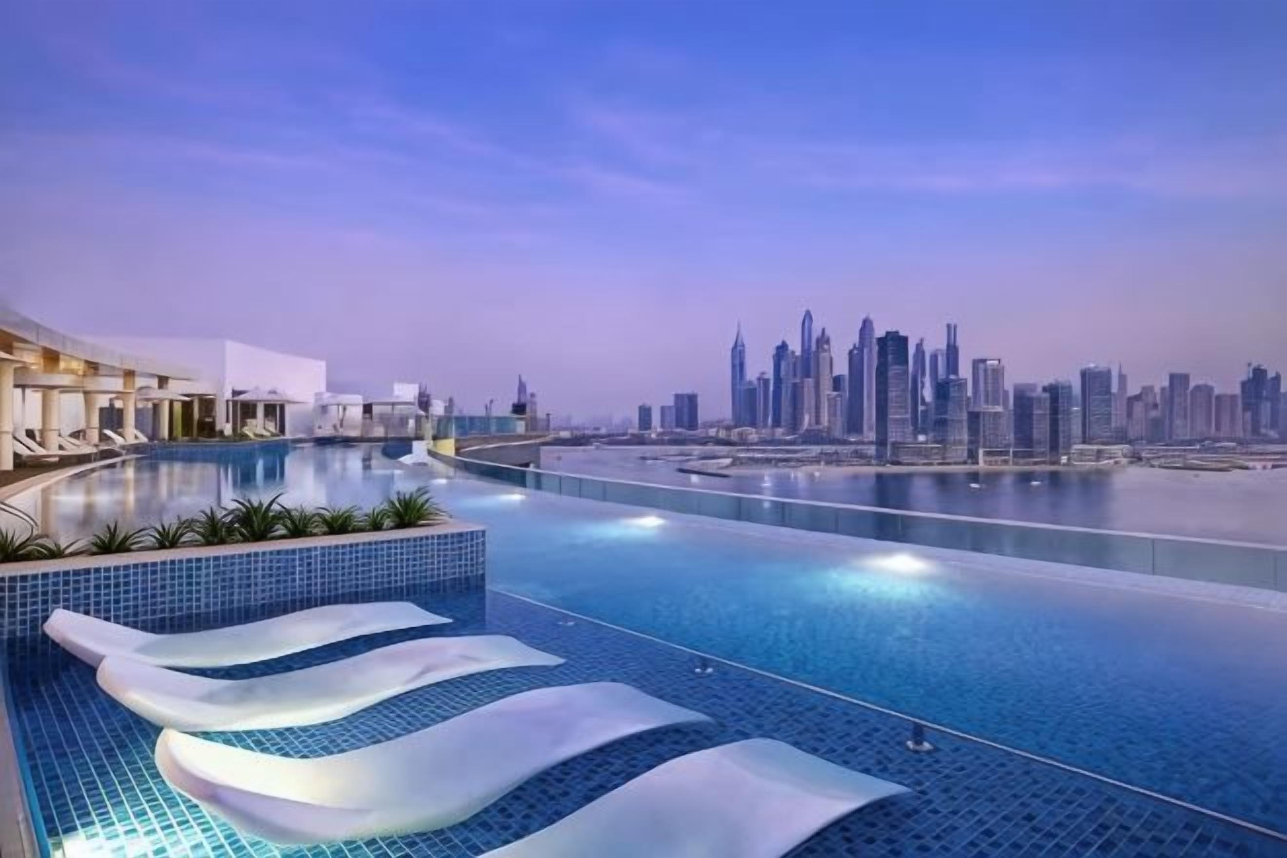 Una piscina moderna de hotel con vistas al horizonte urbano, sillas de descanso y una orilla de agua.