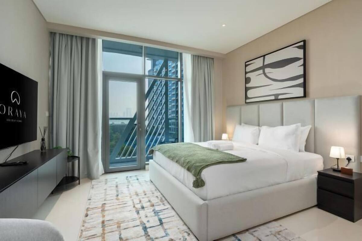 Ein modernes Hotelzimmer mit einem großen Bett, einem Fernseher und Blick auf die Stadt durch ein großes Fenster.
