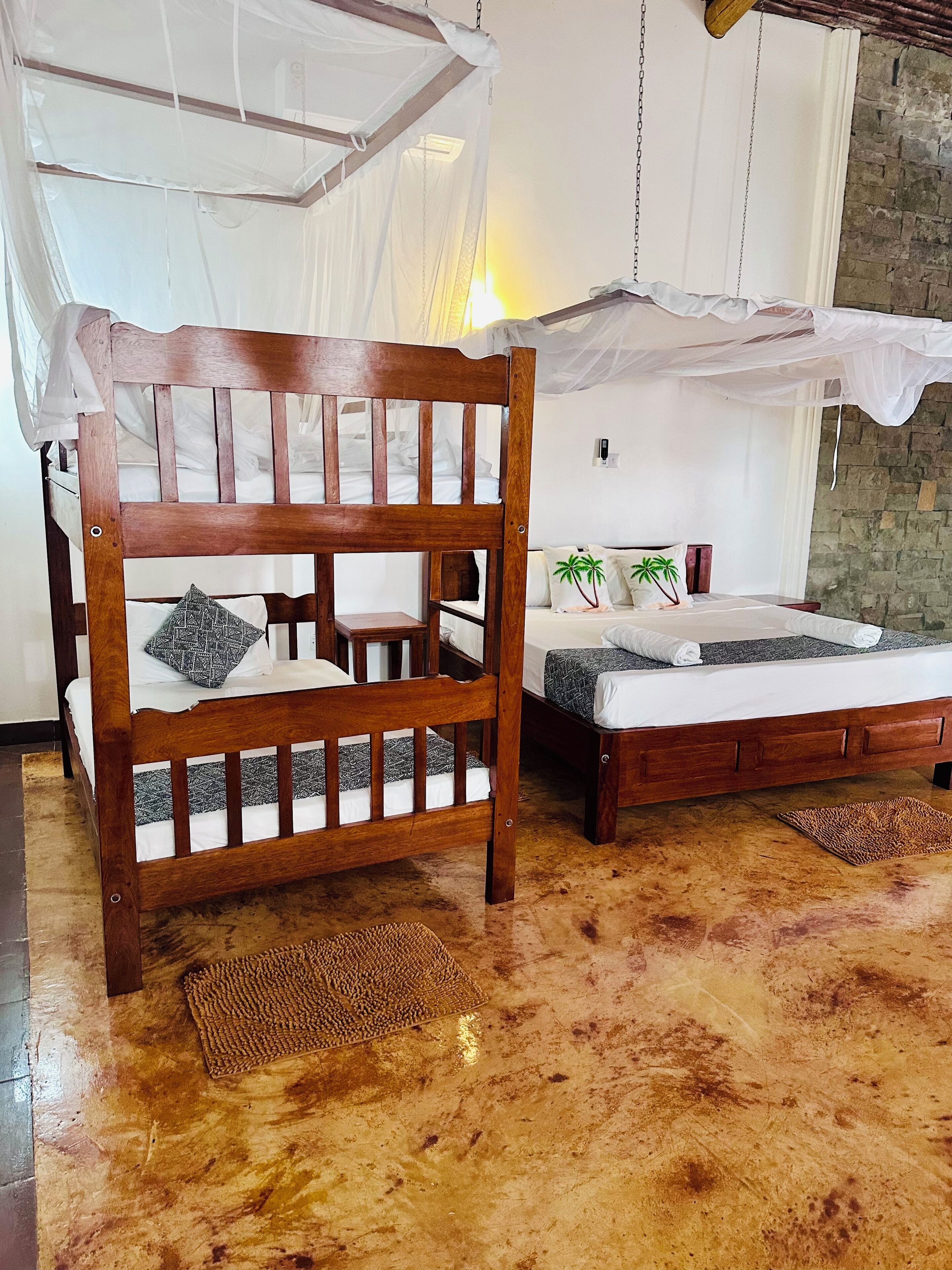 A room with a wooden bed, a smaller bed with a canopy, and a stone wall.